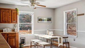 A kitchen with wooden cabinets, a dining table with chairs, a ceiling fan, and large windows with a view of trees. - Secluded Modern-Rustic Cabin with Hot Tub & Sunrise Old Rag Views near Shenandoah National Park, Luray VA (Luray)