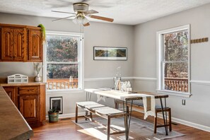 A kitchen with wooden cabinets, a dining table with chairs, a ceiling fan, and large windows with a view of trees. - Secluded Modern-Rustic Cabin with Hot Tub & Sunrise Old Rag Views near Shenandoah National Park, Luray VA (Luray)