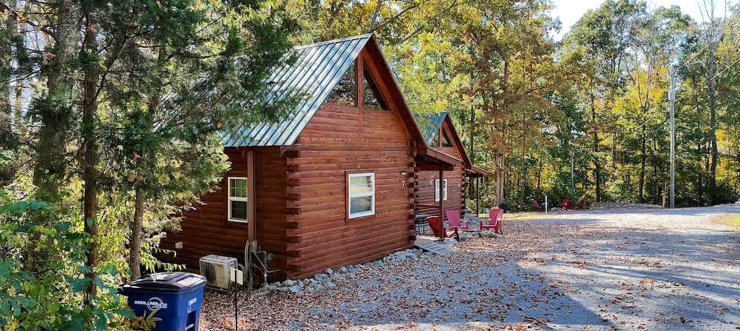 A log cabin with a metal roof, surrounded by trees and gravel.