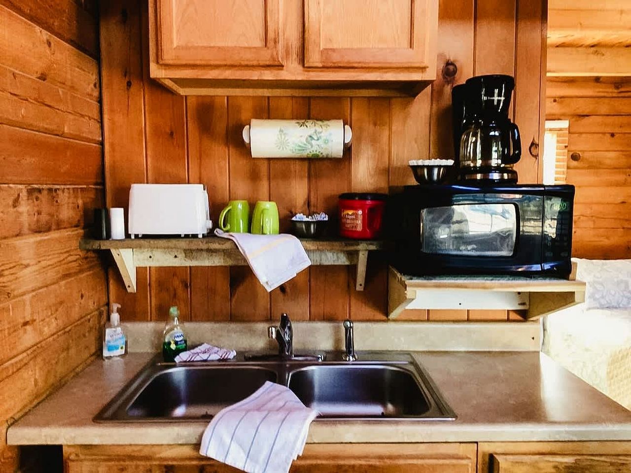 A compact kitchen with wooden cabinets, a microwave, a coffee maker, and a sink.
