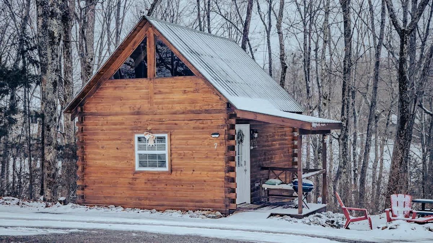 A wooden cabin with a pitched roof, a small porch, and a single window.
