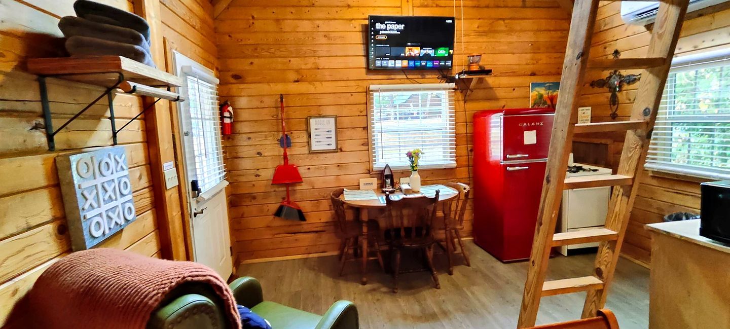 Een compact houten chalet met een eethoek, een rode koelkast en een wandtelevisie.