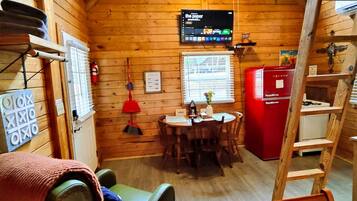 Een compact houten chalet met een eethoek, een rode koelkast en een wandtelevisie.