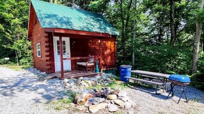 Una cabana de fusta amb un porxo, una barbacoa i una zona amb foc.