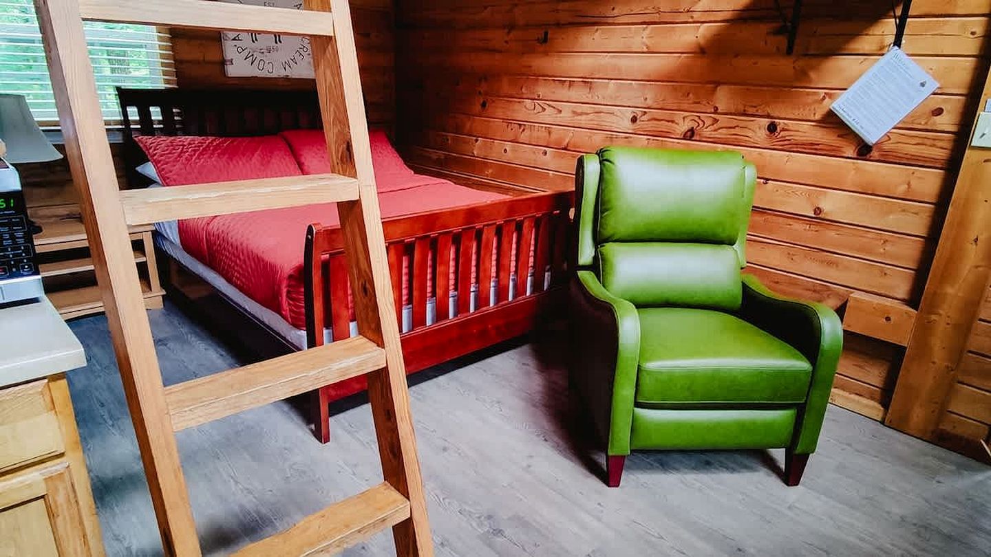 A wooden room with a bunk bed, a green chair, and a ladder.