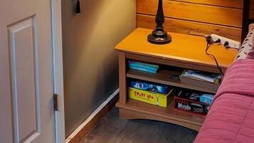 Een knus interieur met een houten plafond, een bed met een roze deken, een nachtkastje met een lamp en planken met boeken en een decoratief object.