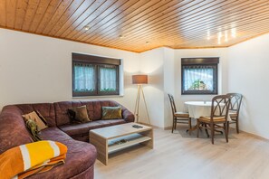 A living room with a wooden ceiling, a sofa, a coffee table, a lamp, and a dining area with chairs and a table.