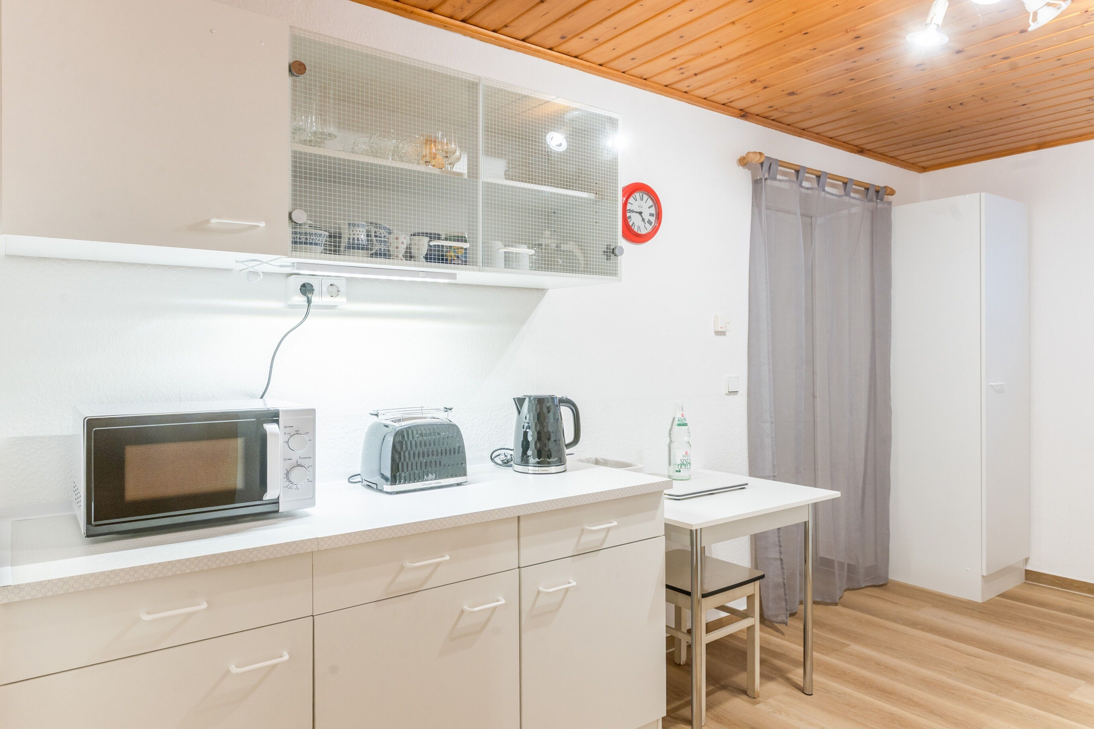 Eine Küchenzeile mit Mikrowelle, Toaster, Wasserkocher und einem kleinen Tisch mit Stuhl.