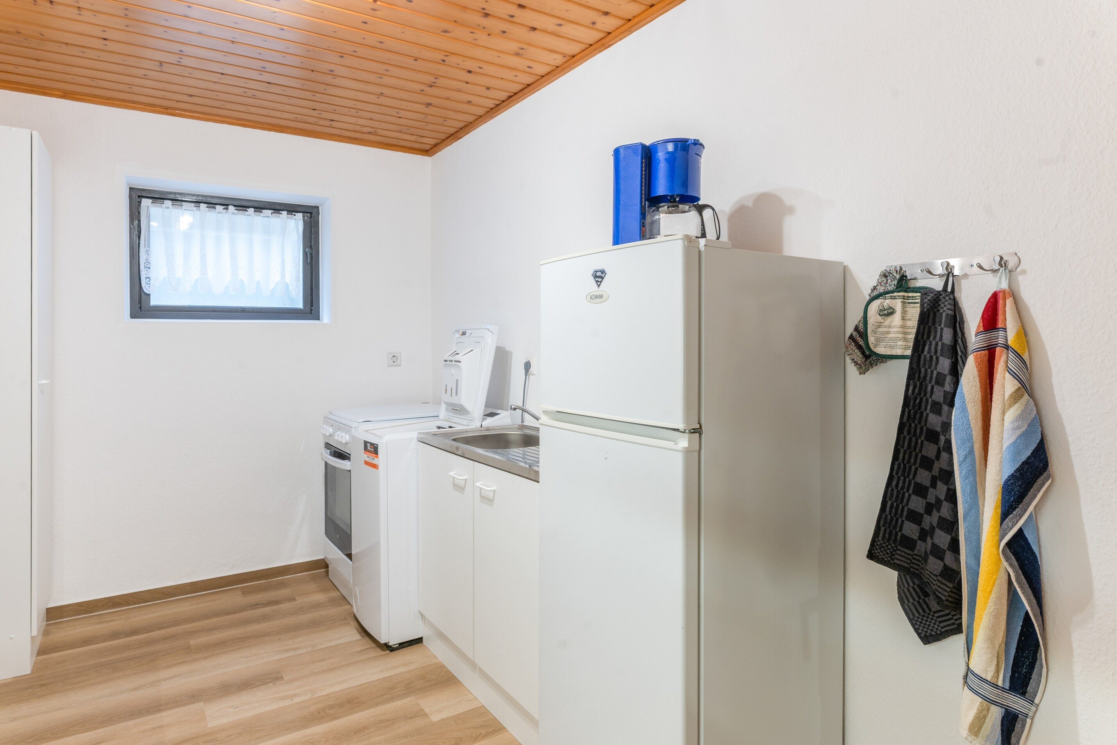 Une cuisine de taille réduite, équipée d’un réfrigérateur, d’un lave-linge et d’une petite fenêtre.