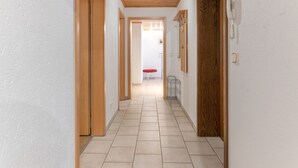A corridor with wooden doors and a tiled floor leading to a room with a red chair and a table. - Apartment 'Auszeit im Grünen' with Mountain View, Shared Garden and Wi-Fi (Plaue)