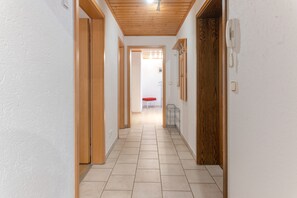 A corridor with wooden doors and a tiled floor leading to a room with a red chair and a table.