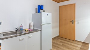A small kitchenette with a white refrigerator, a coffee maker, a sink with a faucet, and a wooden door. - Apartment 'Auszeit im Grünen' with Mountain View, Shared Garden and Wi-Fi (Plaue)