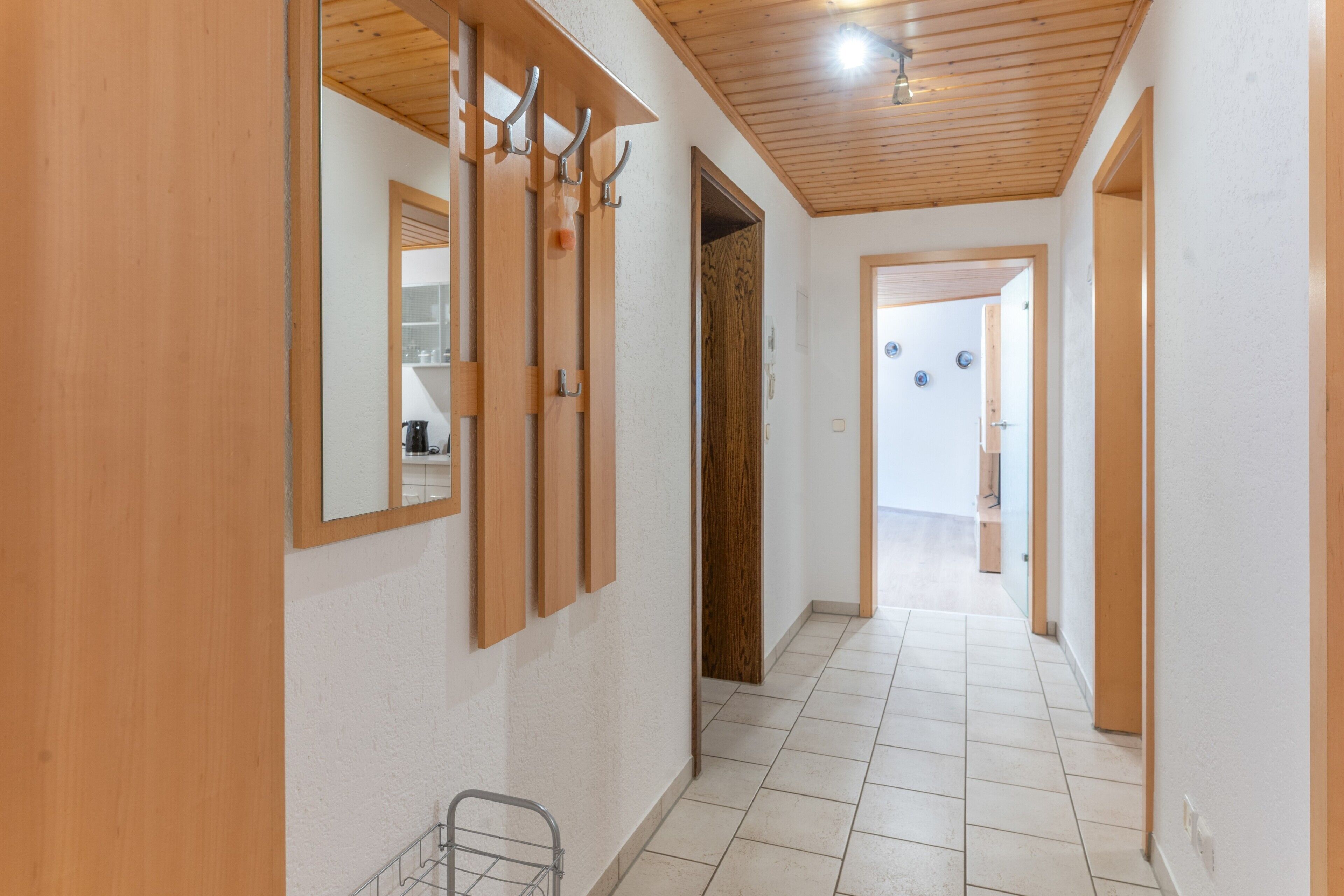 Un couloir avec un plancher en bois, un miroir et une porte.