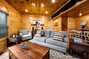 L’intérieur chaleureux d’un chalet comprend un canapé, un fauteuil, une table basse en bois et un coin repas avec des chaises et une table.