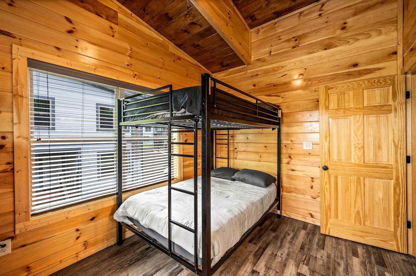 A bunk bed room with wooden walls and a window with blinds.