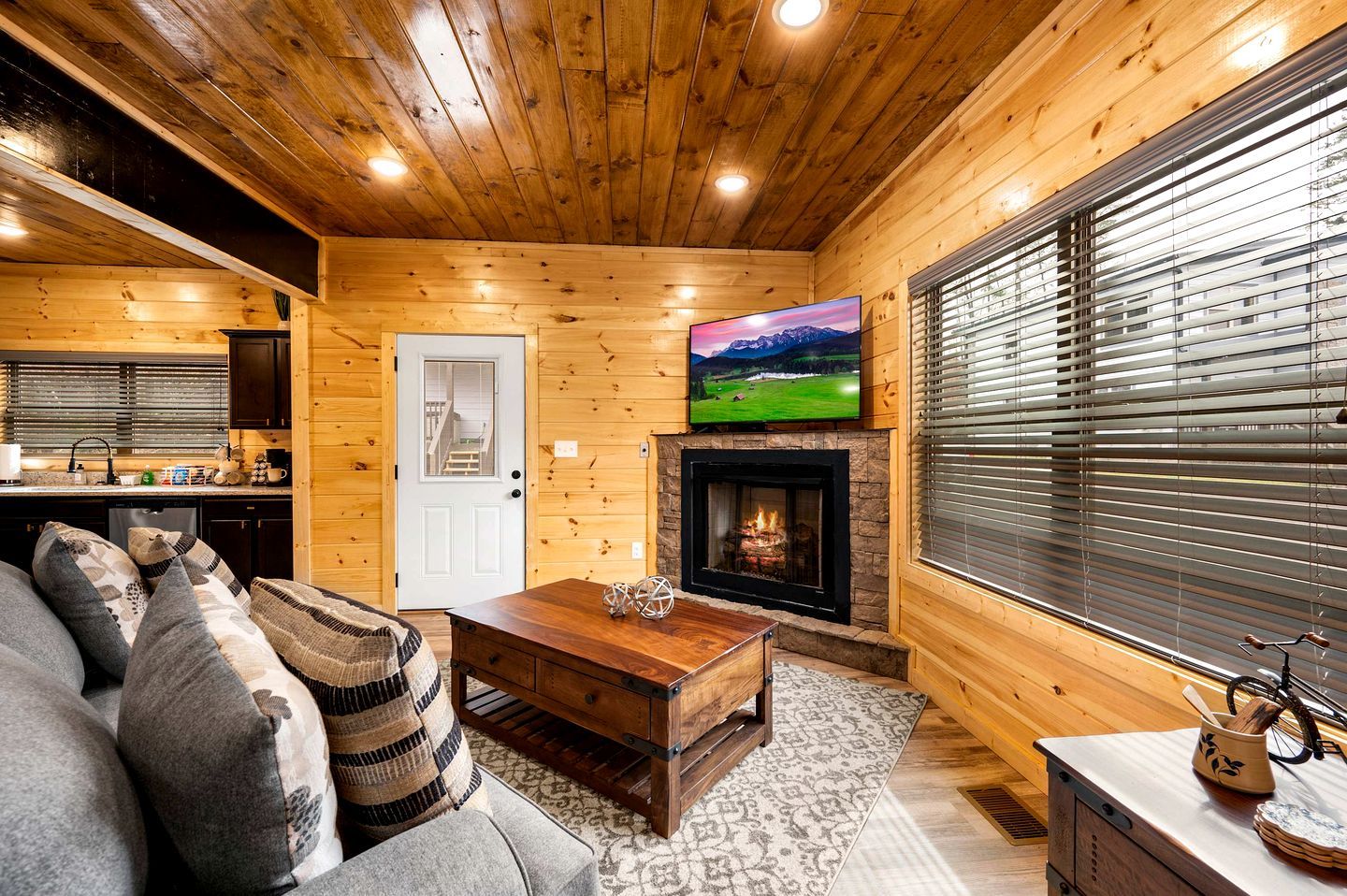 A cozy cabin interior with a wooden interior, a fireplace, a television, and a sofa with cushions.