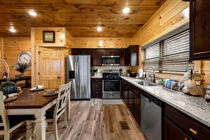 Une cuisine de style rustique, avec des murs en bois, un réfrigérateur en acier inoxydable, un four à micro-ondes, une cuisinière et un évier.