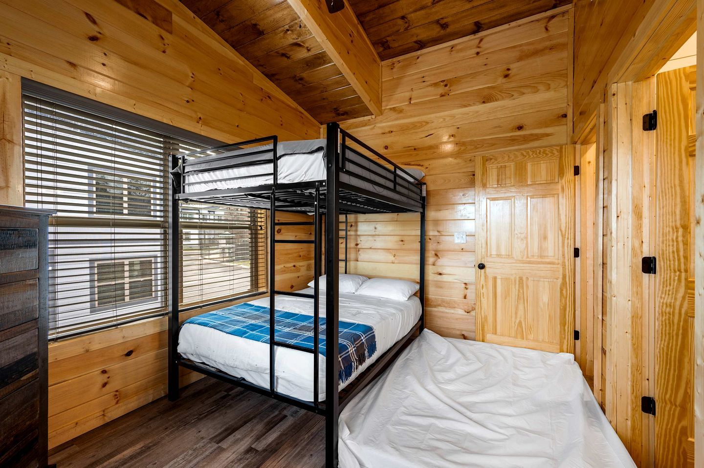 A bunk bed room with wooden walls and a window with blinds.