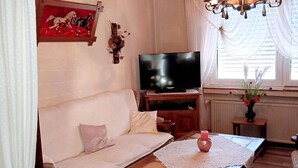 Ett vardagsrum med en soffa, en tv, ett träbord och en kristallkrona.