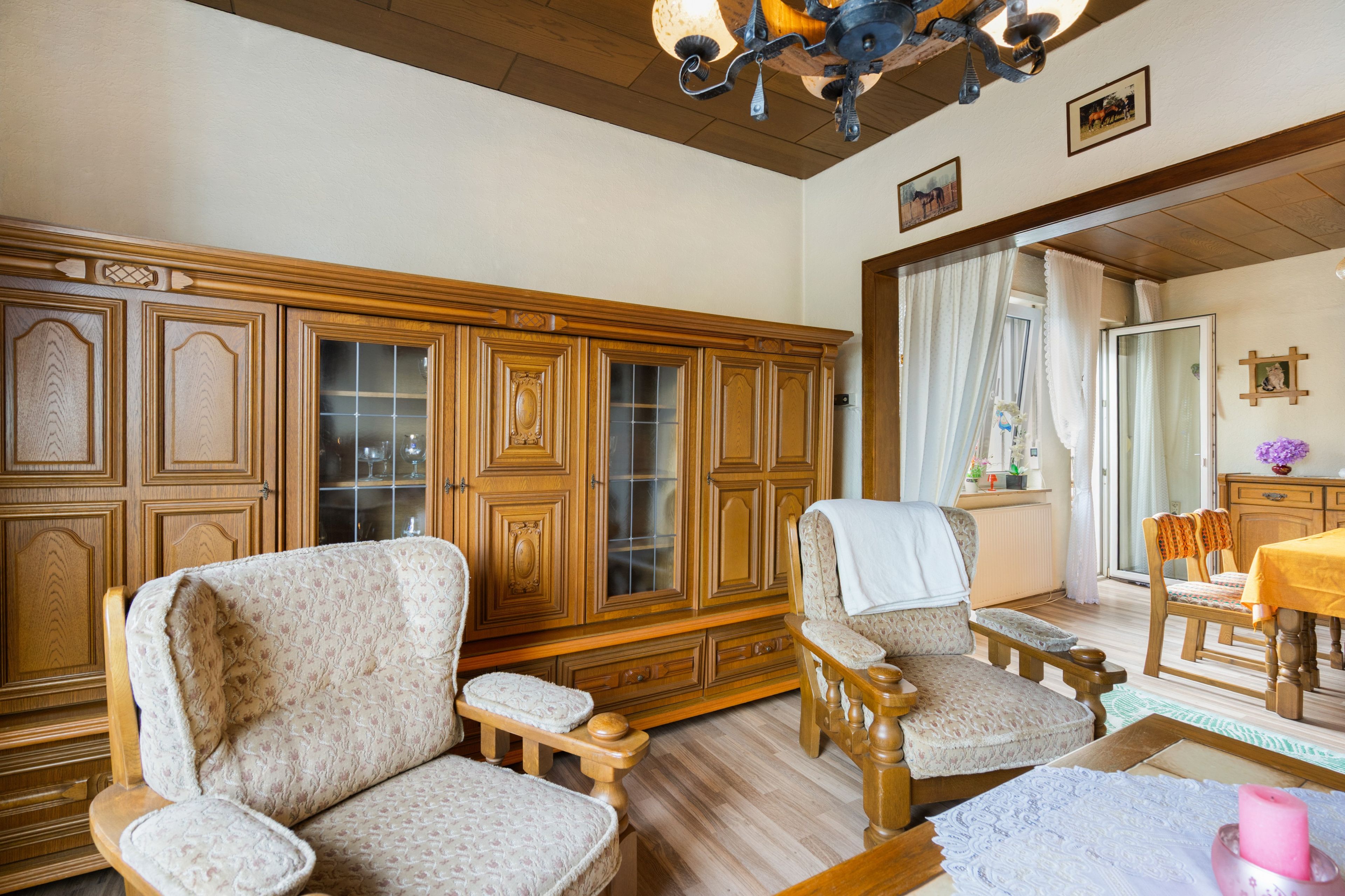 A room with wooden furniture, including a cabinet with glass doors and two upholstered chairs.
