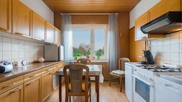 A kitchen with wooden cabinets, a dining table with chairs, a window with curtains, and a stove.