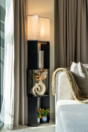 A modern living room with a black floor lamp, a white vase with flowers, and a grey sofa with a patterned throw. - Gogoto9 Spacious 3BR Burj Khalifa view High Floor (Dubai)