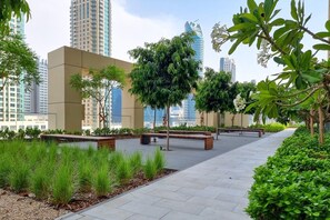 A landscaped urban walkway with benches, trees, and a view of high-rise buildings. - Gogoto9 Spacious 3BR Burj Khalifa view High Floor (Dubai)
