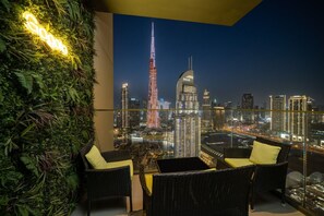 A balcony with a view of the Burj Khalifa and other buildings, two wicker chairs, a small table, and a green wall with plants. - Gogoto9 Spacious 3BR Burj Khalifa view High Floor (Dubai)