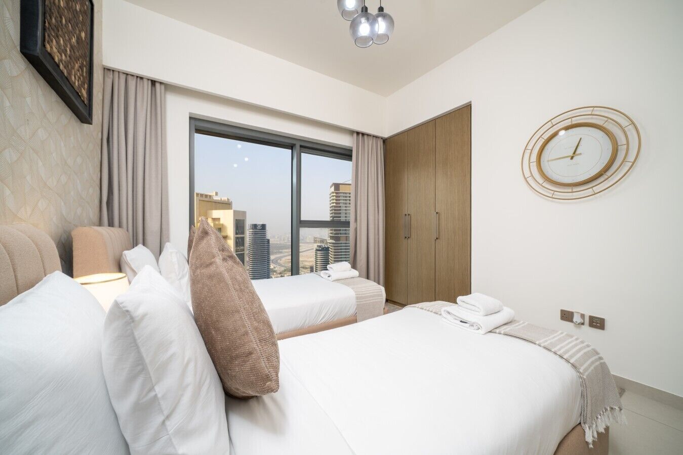 Habitación de hotel con dos camas, un ventanal grande, un armario y un reloj de pared.