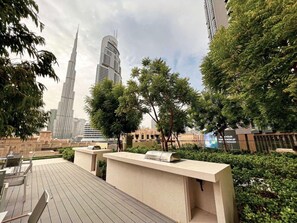 Eine Dachterrasse mit Sitzgelegenheiten im Freien, einem Grill und Blick auf den Burj Khalifa.