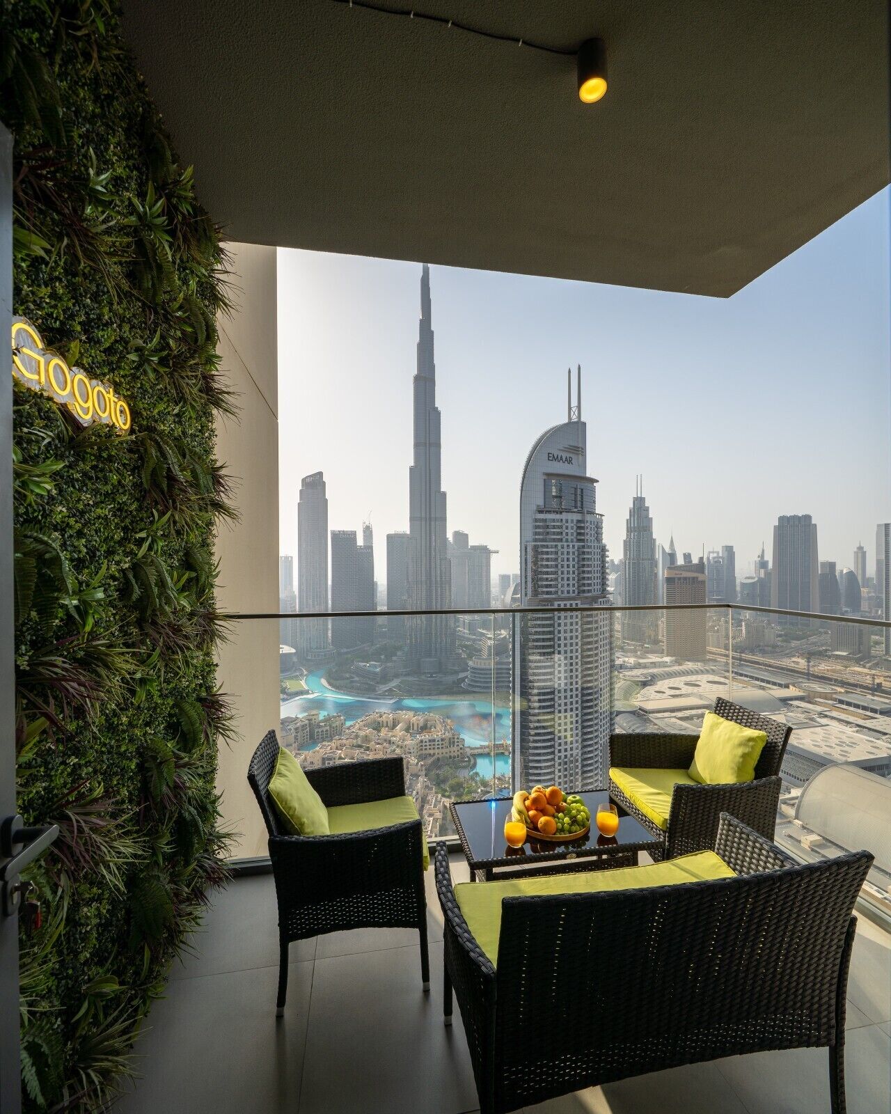 Un balcon offrant une vue sur le Burj Khalifa et sur les autres bâtiments emblématiques de Dubaï, aménagé avec des fauteuils en osier et une table sur laquelle sont disposés des fruits.