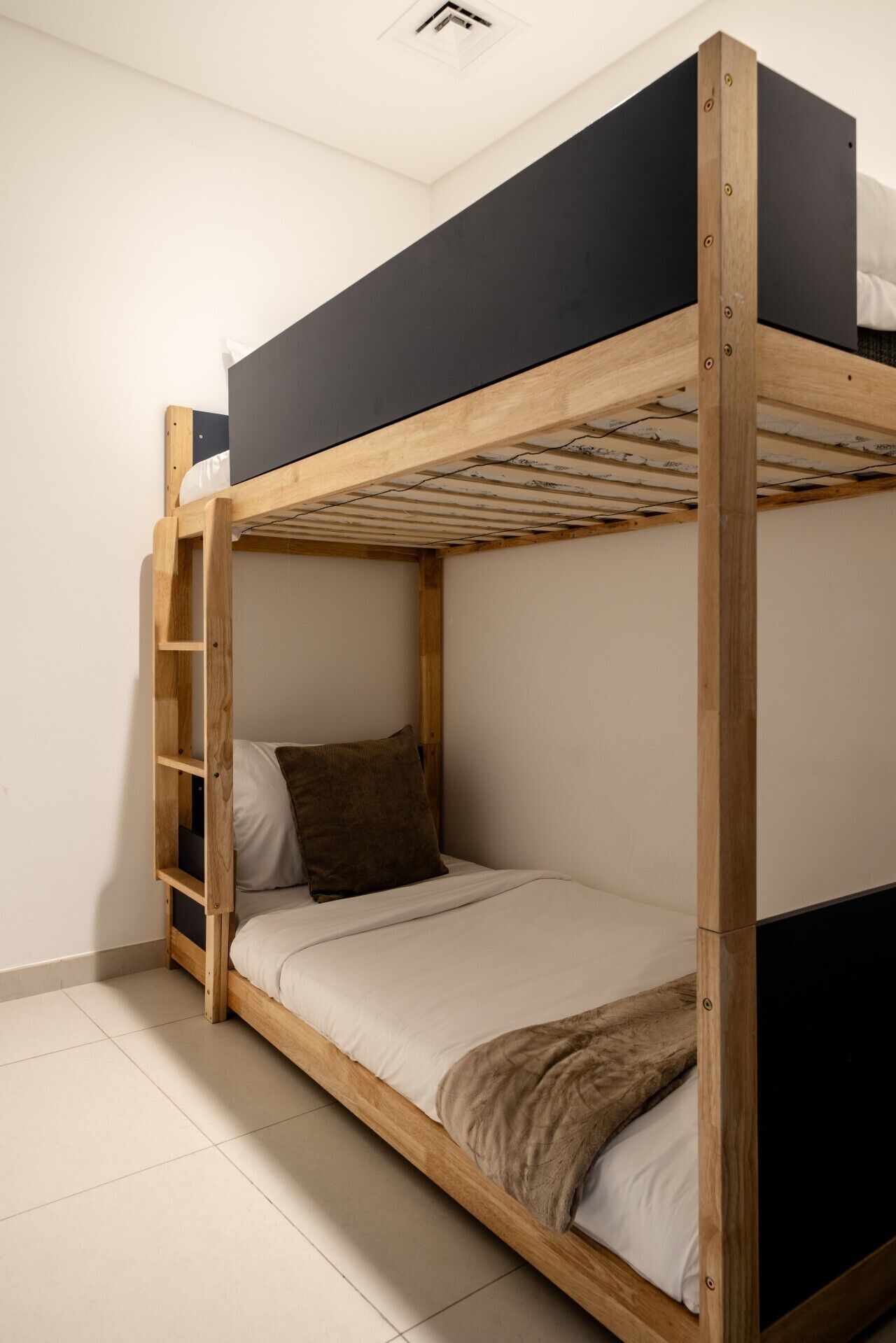 Un lit superposé avec une structure en bois, un matelas noir sur le lit du haut et un matelas blanc sur le lit du bas.