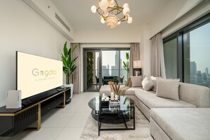 A modern living room with a large TV, a sofa, a coffee table, and a city view. - Gogoto9 Spacious 3BR Burj Khalifa view High Floor (Dubai)