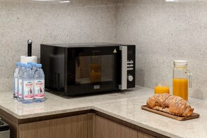 A kitchen with a microwave, water bottles, a glass of orange juice, and a loaf of bread on a wooden board. - Gogoto9 Spacious 3BR Burj Khalifa view High Floor (Dubai)