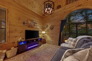 Ein gemütliches Blockhauss-Interieur mit einem großen Flachbildfernseher, einem Kamin und einer komfortablen Sitzecke.