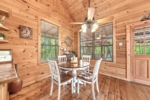 Ein Holzblockbau-Innenraum mit Esstisch, Stühlen, Deckenventilator und großen Fenstern.