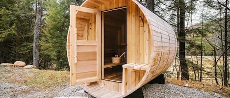 A wooden sauna with a curved roof, open door, and benches inside, set in a forest.