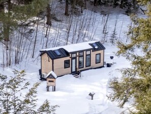 A cabin with a sloped roof, large windows, and a snow-covered ground. - Stunning Cedar Tiny House with Sauna Access for a Romantic Getaway in Chester, Vermont (Chester)