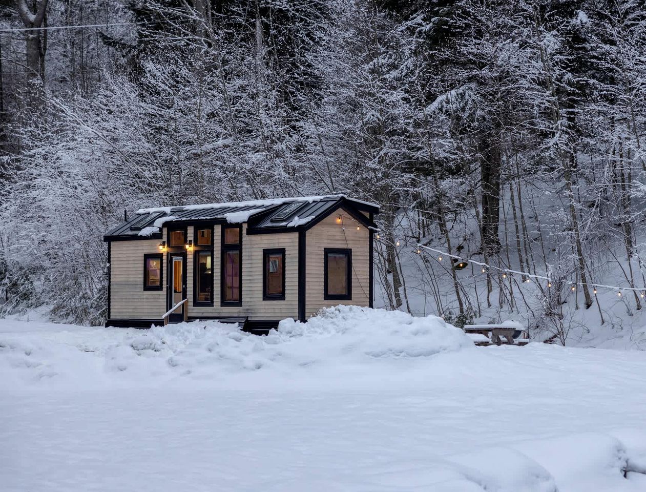 Une petite cabane dotée d’un porche, entourée d’arbres couverts de neige.