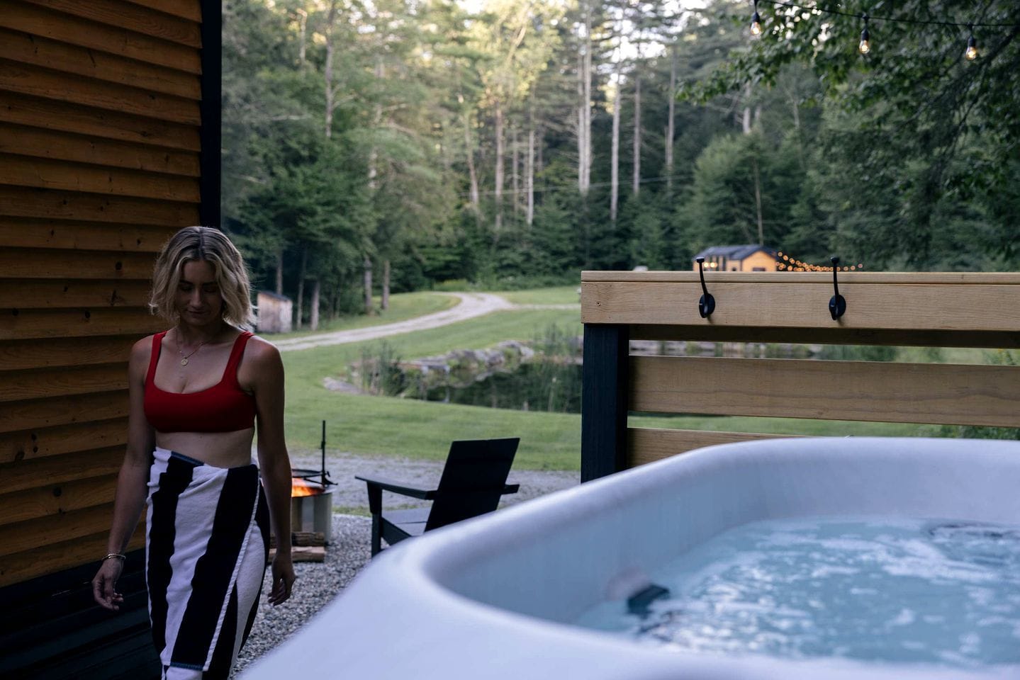 Eine Person steht an einer Holzterrasse. Im Vordergrund befindet sich ein Whirlpool, im Hintergrund eine bewaldete Landschaft.