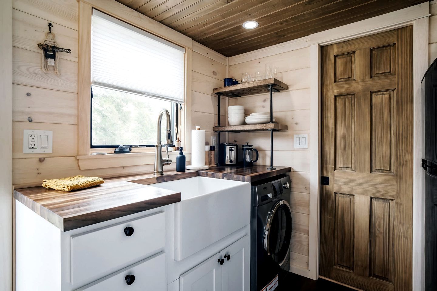 A compact kitchen with a sink, a washing machine, and wooden shelves.