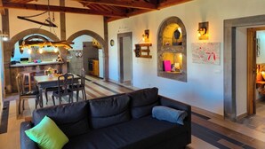 Ein gemütliches Interieur mit Holzbalkendecke, einem Essbereich, einer Couch und einer im Hintergrund erkennbaren Küche.