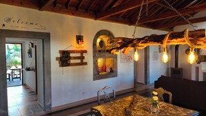 Ein rustikales Interieur mit Holzbalkendecke, einem Willkommensschild, einem Steinkamin und einem Essbereich mit Tisch und Stühlen.