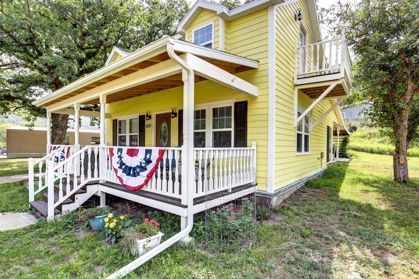 A yellow house with a porch, a small garden, and a mailbox.