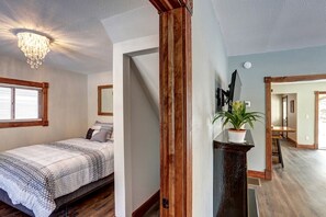 A bedroom with a bed, a window with blinds, a chandelier, and a plant on a stand. - Enchanting Historic Cabin Retreat near Mount Rushmore in South Dakota (Keystone)