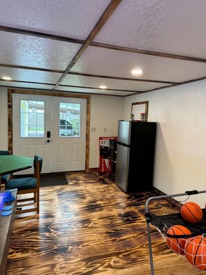 A room with a wooden floor, a table with chairs, a refrigerator, and a door leading outside. - Enchanting Historic Cabin Retreat near Mount Rushmore in South Dakota (Keystone)