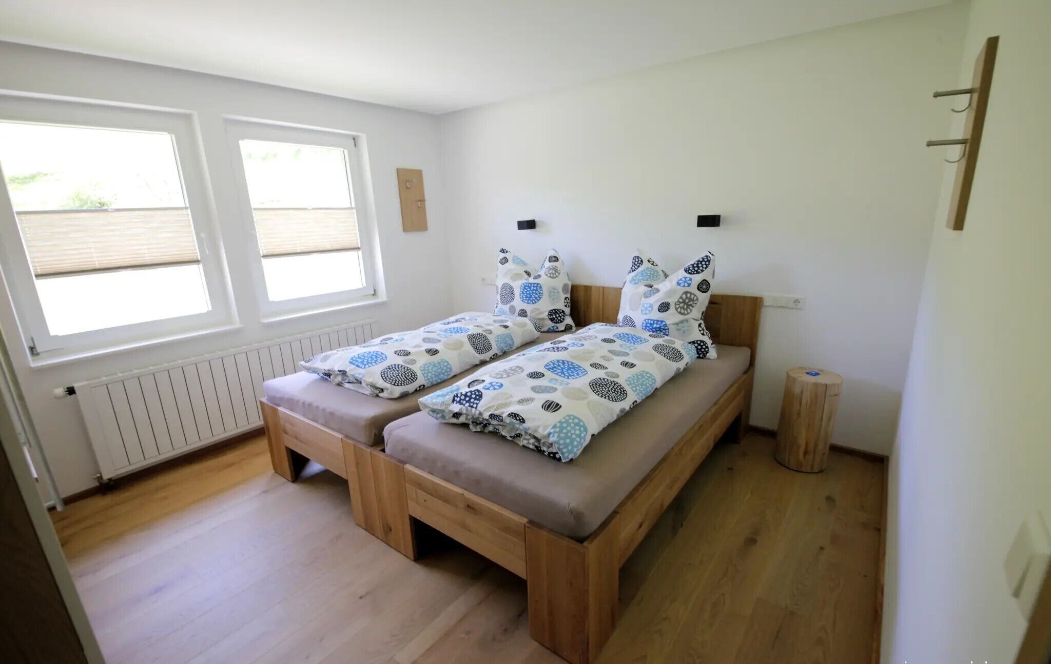 A small, bright room with two wooden beds, a window, and a radiator.