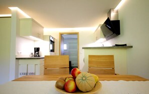 A small room with a dining table, chairs, a television, and a kitchen area in the background. - Apartment 'Abendgrund' with Private Terrace, Shared Garden and Wi-Fi (Unterkirnach)