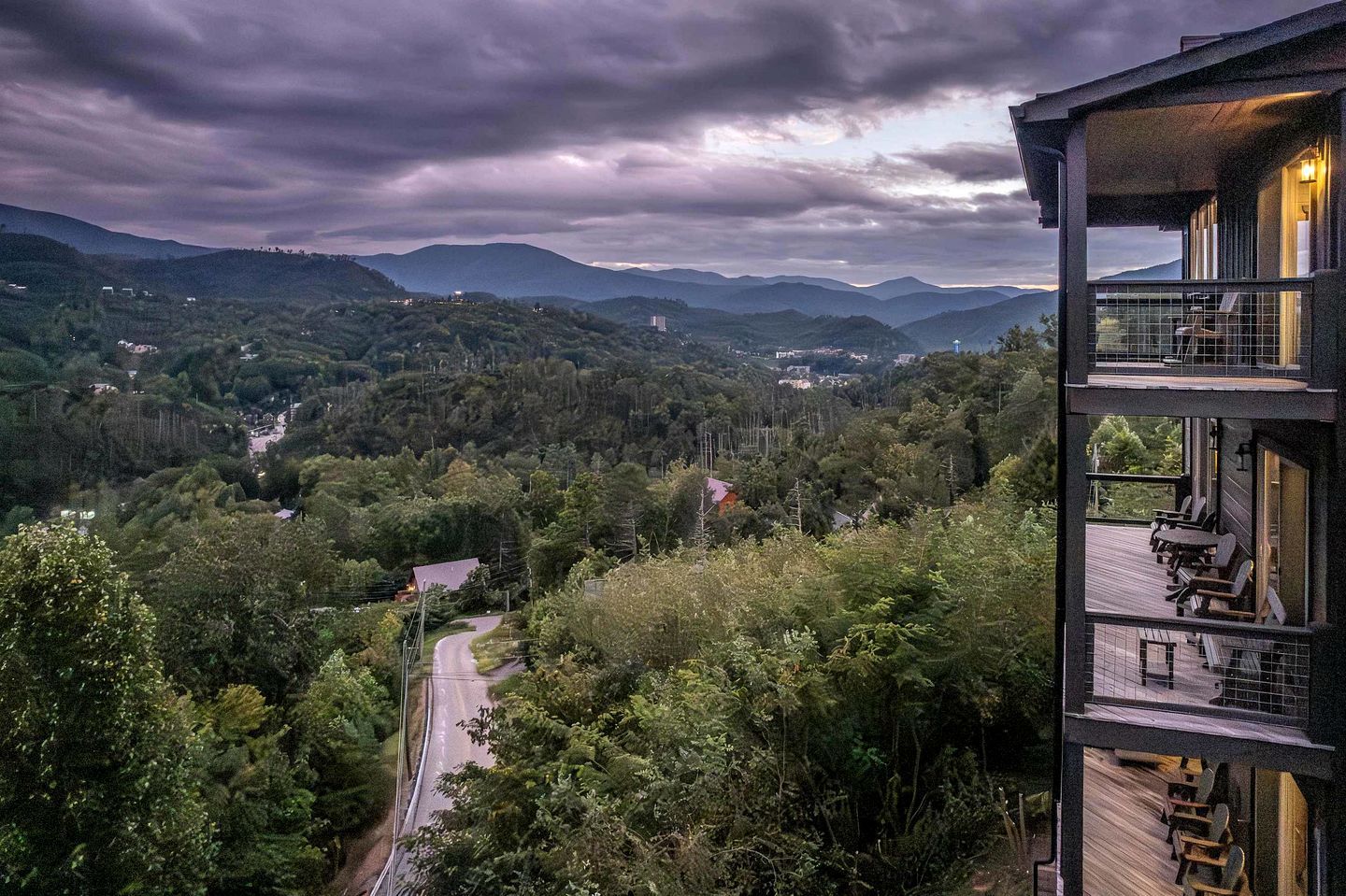 Un immeuble à plusieurs étages doté d’un balcon donnant sur une vallée boisée et sur des montagnes lointaines.