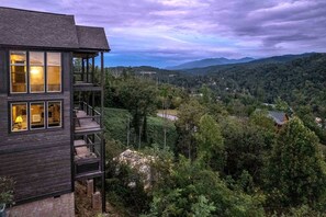 A multi-story wooden cabin with a balcony, surrounded by dense forest and mountains. - Scenic Smoky Mountain Cabin with Theater & Game Room near Gatlinburg, Tennessee (Gatlinburg)
